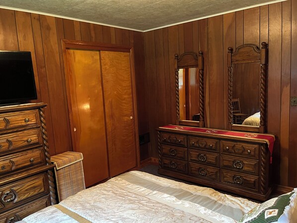 Un dormitorio con paneles de madera, un aparador con cajones, un espejo y un televisor sobre un mueble bajo.
