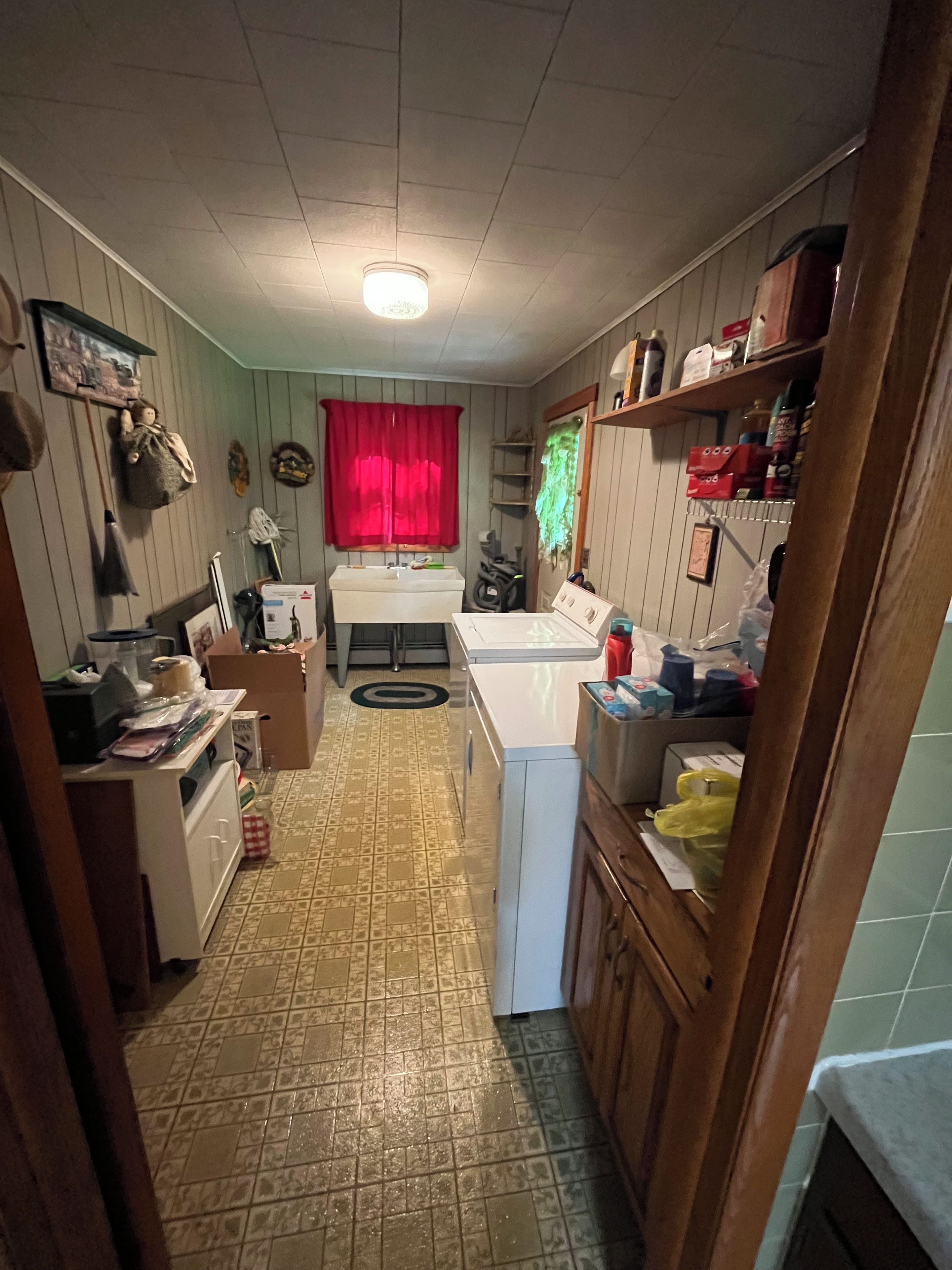 A compact kitchen with a sink, stove, and a window with a red curtain.