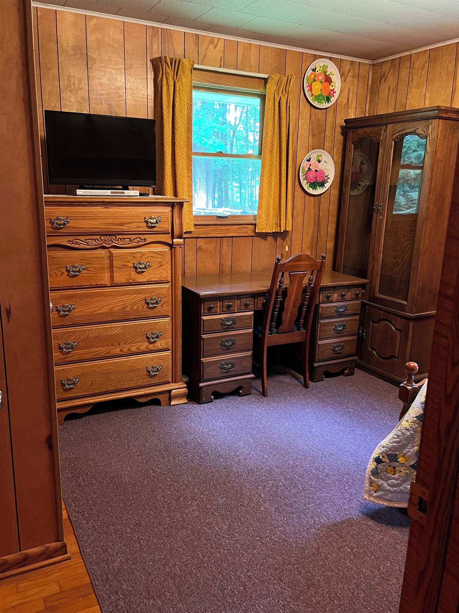 A room with a wooden dresser, a television, a desk, and a chair.