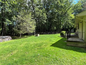 A well-maintained lawn with a stone wall, a small bush, and a building with a porch.