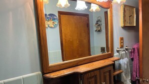 Casa de banho com toucador de madeira, espelho grande e relógio fixado na parede.