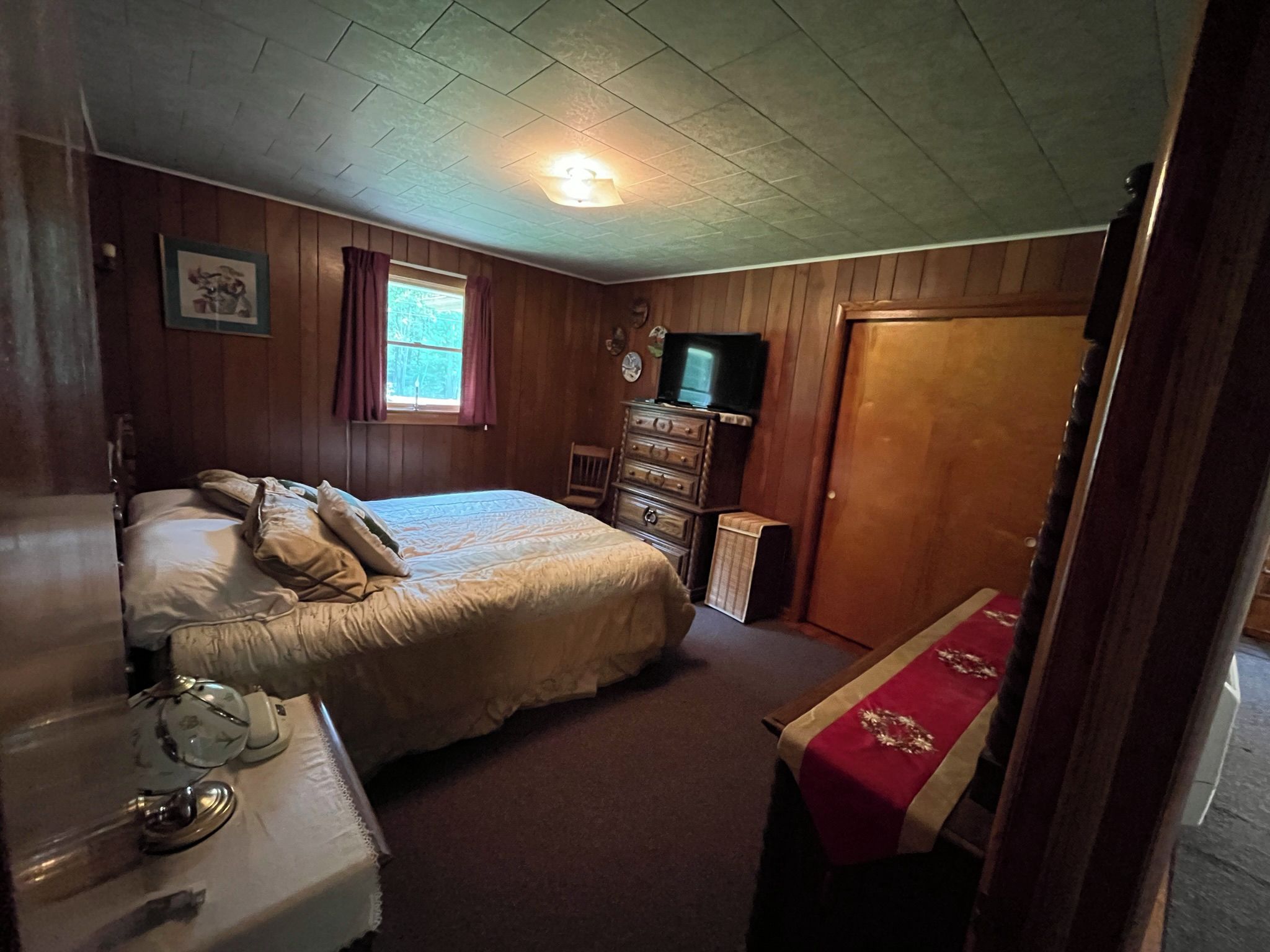 Une chambre à coucher avec un lit, une commode, une télévision et une fenêtre avec des rideaux.