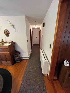 Un pasillo con piso de madera, un radiador y una puerta a la derecha.