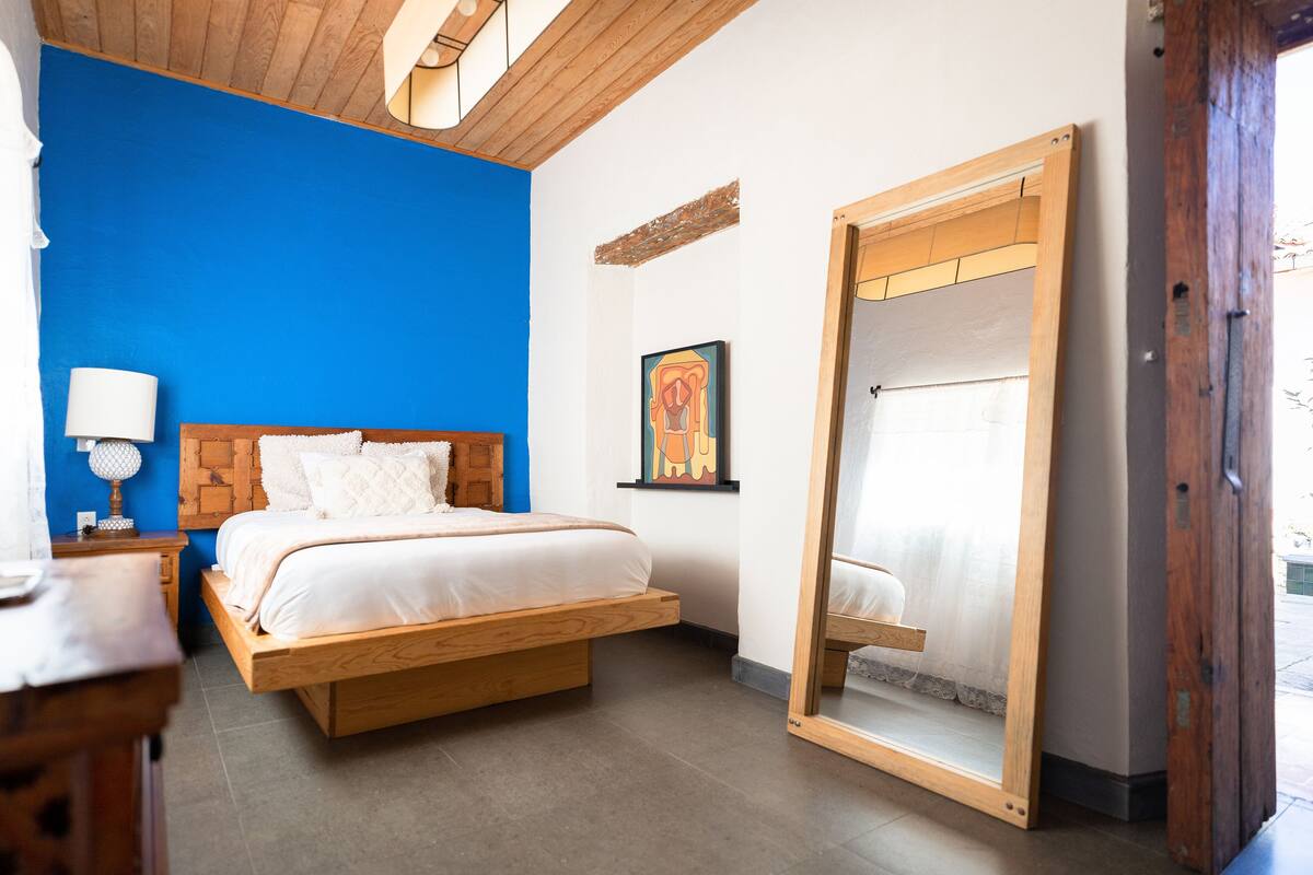 A bedroom with a bed, a nightstand, a mirror, and a blue accent wall.