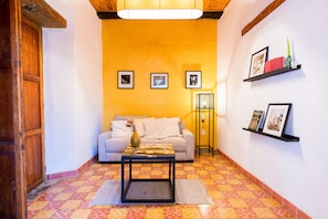 A living room with a sofa, a coffee table, and a floor lamp. There are three framed pictures on the wall and a shelf with books and a vase. - Casa I Madero (Tapalpa)