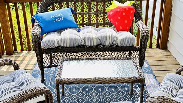 Un canapé en osier avec des coussins à rayures et un coussin bleu, une table en osier assortie et des chaises assorties, le tout posé sur un tapis bleu à motifs.