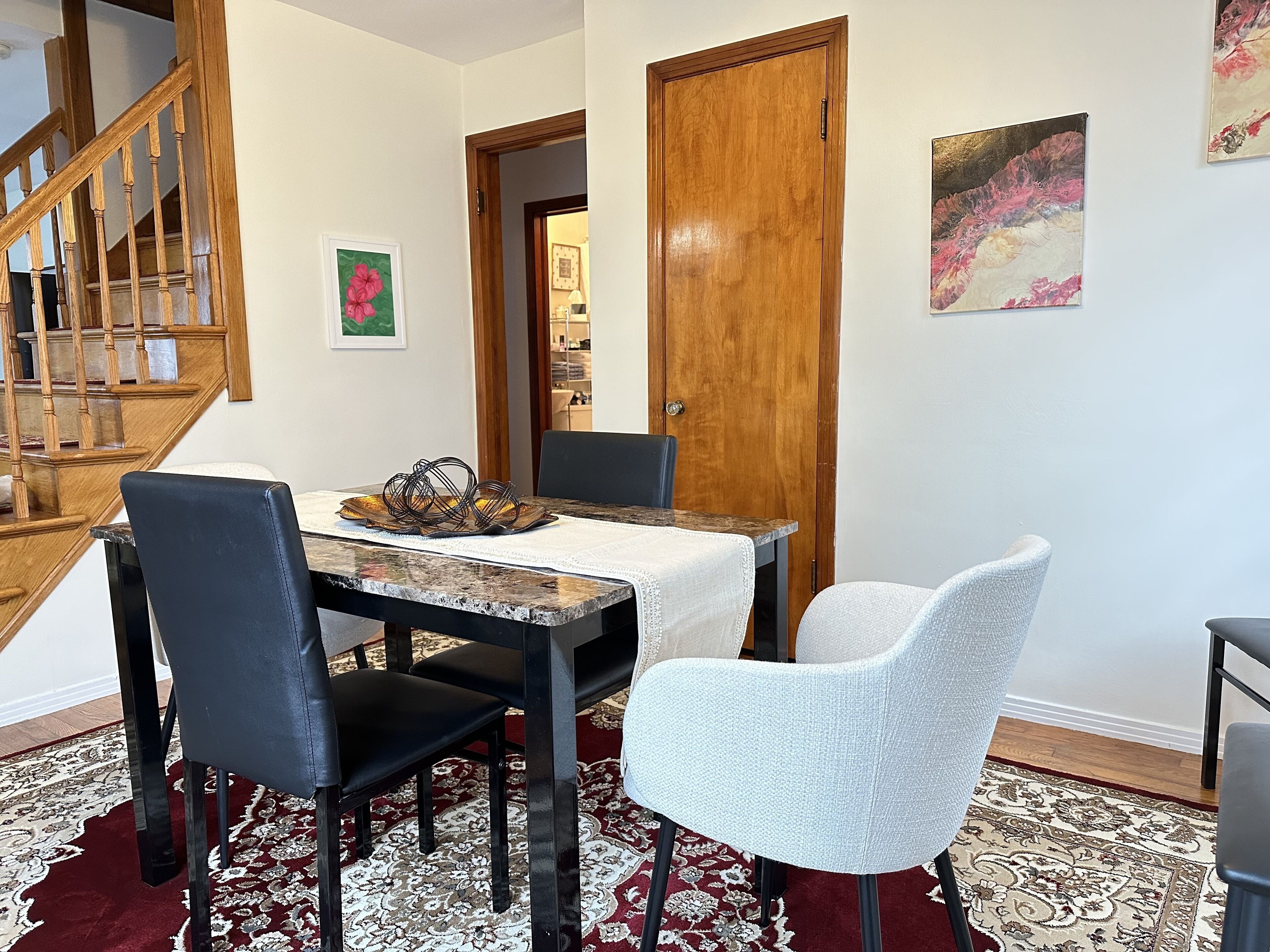 Un coin repas avec une table en bois, deux chaises, un tapis et un escalier.