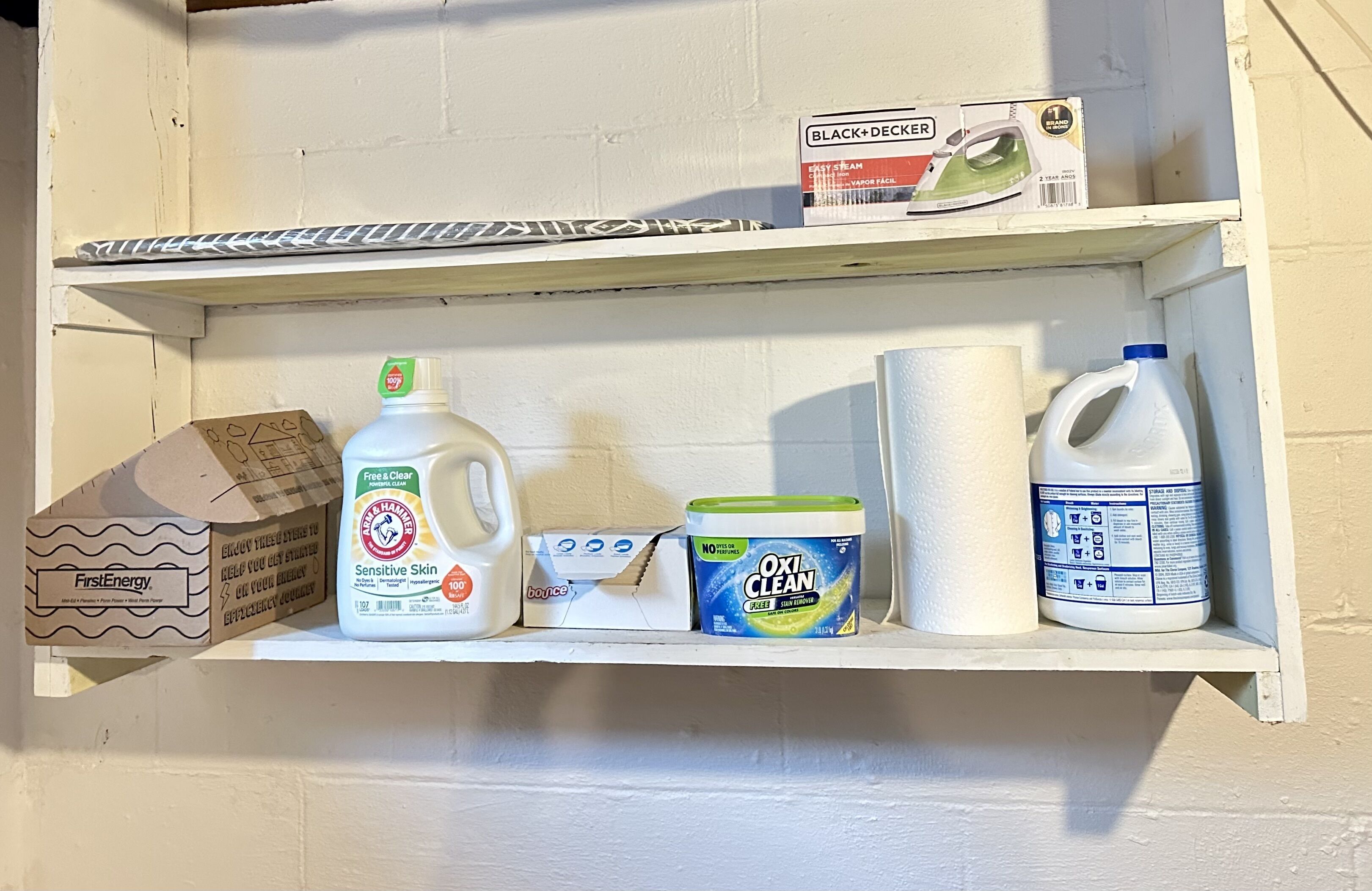 Une étagère contenant divers produits de nettoyage, notamment une bouteille de lait, un flacon de liquide vaisselle et une boîte de serviettes en papier.