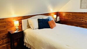 Un lit bien fait, avec une couette blanche, une tête de lit en bois et une table de chevet sur laquelle se trouve une lampe.