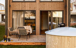 Eine Holzterrasse mit Gartenmöbeln, einem Whirlpool und Blick ins Haus.