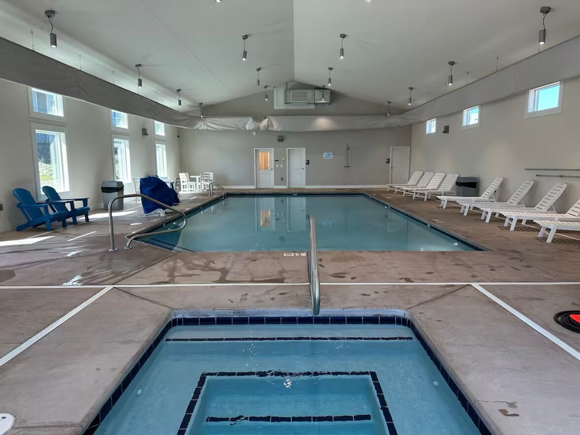 Une piscine intérieure à l’eau claire, entourée de chaises longues et dotée d’un sol carrelé.