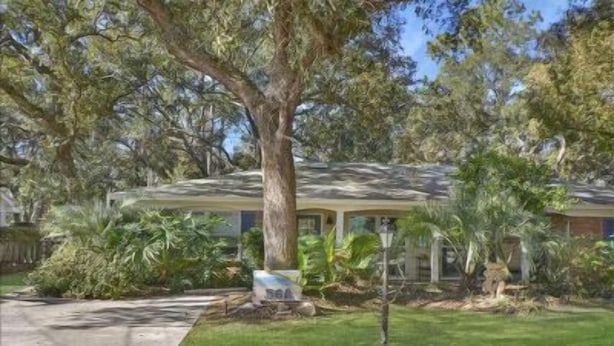A single-story house with a covered porch, surrounded by lush greenery and a well-maintained lawn. - All Wright : 2 BR, 1 BA Duplex in Jekyll Island, Sleeps 4 (Jekyll Island)