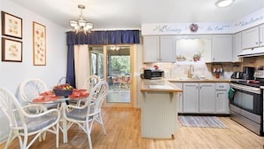 A compact kitchen with white cabinets, a central island, and a dining area with white chairs. - All Wright : 2 BR, 1 BA Duplex in Jekyll Island, Sleeps 4 (Jekyll Island)
