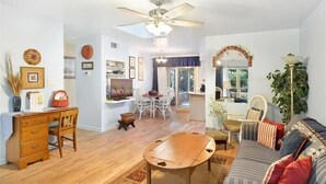 A spacious living room with a wooden coffee table, a sofa with patterned cushions, a dining area with chairs, and a ceiling fan. - All Wright : 2 BR, 1 BA Duplex in Jekyll Island, Sleeps 4 (Jekyll Island)