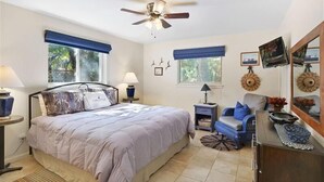 A bedroom with a bed, a ceiling fan, a nightstand, a dresser, a chair, and a window with blue curtains. - All Wright : 2 BR, 1 BA Duplex in Jekyll Island, Sleeps 4 (Jekyll Island)
