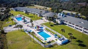 Luftaufnahme eines Resorts mit mehreren Schwimmbecken, Liegestühlen und einem großzügigen Gebäude mit gewölbtem Dach.