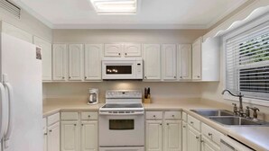 Une cuisine avec des meubles blancs, un four à micro-ondes, une cuisinière et un évier.