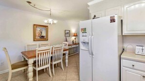Une cuisine avec des meubles blancs, un réfrigérateur, un grille-pain et une table à manger avec des chaises.