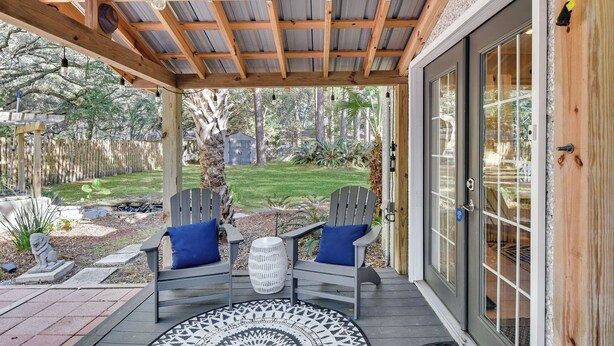 A covered patio with two Adirondack chairs, a round table, and a view of the backyard.