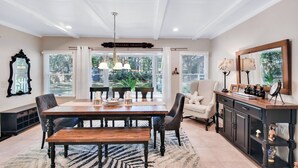 A dining area with a wooden table, chairs, and a bench. There is a chandelier above the table and a large mirror on the wall.