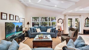 A living room with a large flat-screen TV, a blue sofa, a brown armchair, and a coffee table.