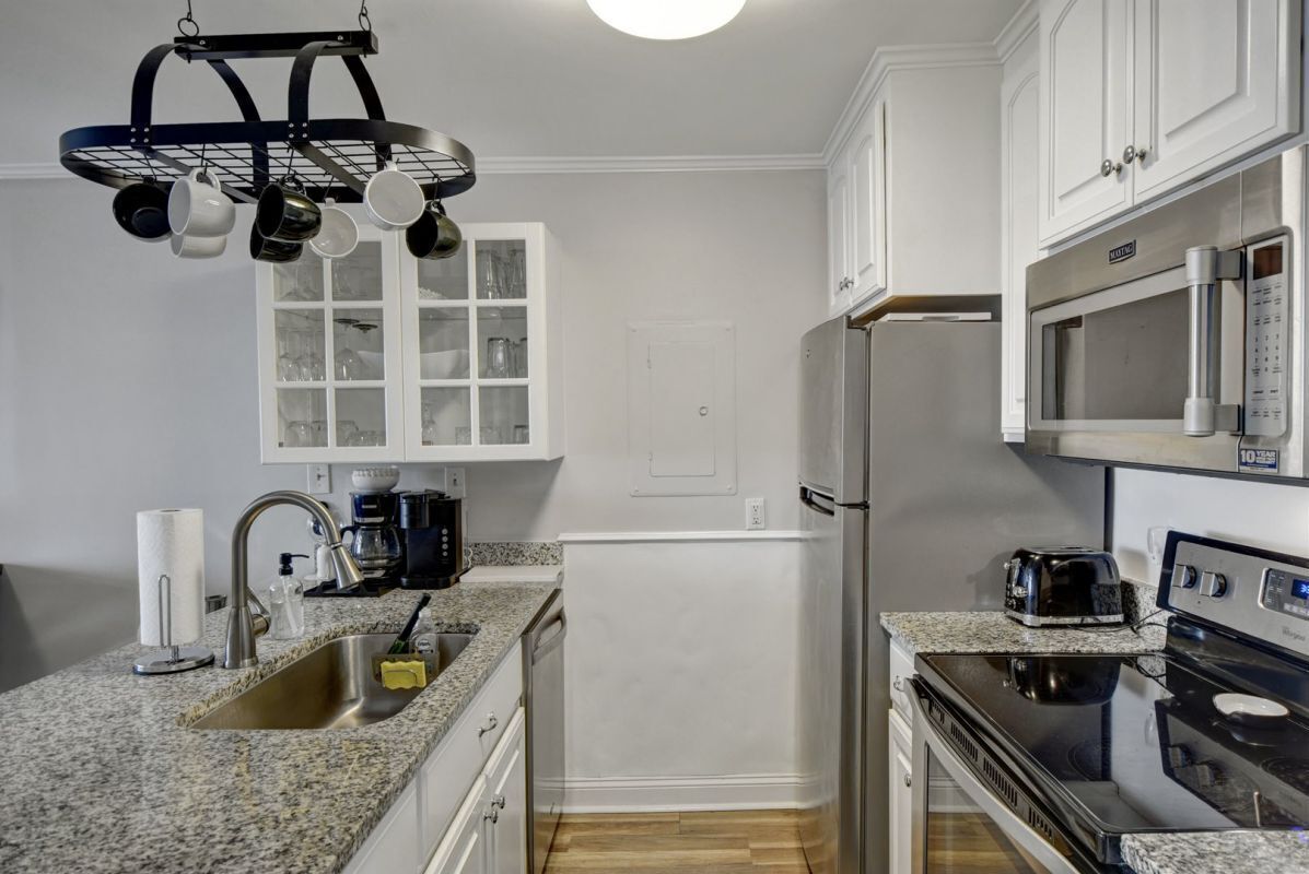 Una cocina compacta con gabinetes blancos, un lavamanos de acero inoxidable, un microondas y una estufa.