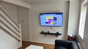 Una sala de estar con una mesa blanca, un sofá negro y un televisor montado en la pared.