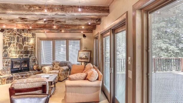A cozy living room with a stone fireplace, a sofa, and a dining area. - Charming 3-bedroom chalet right off the ski slopes! (Lead)