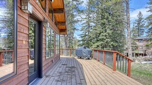 A wooden deck with a covered grill, large windows, and a view of surrounding trees. - Charming 3-bedroom chalet right off the ski slopes! (Lead)
