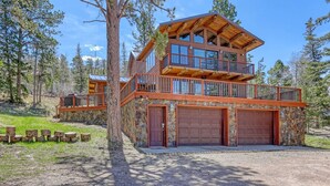 A two-story log cabin with a stone foundation, a wooden deck, and a garage. - Charming 3-bedroom chalet right off the ski slopes! (Lead)
