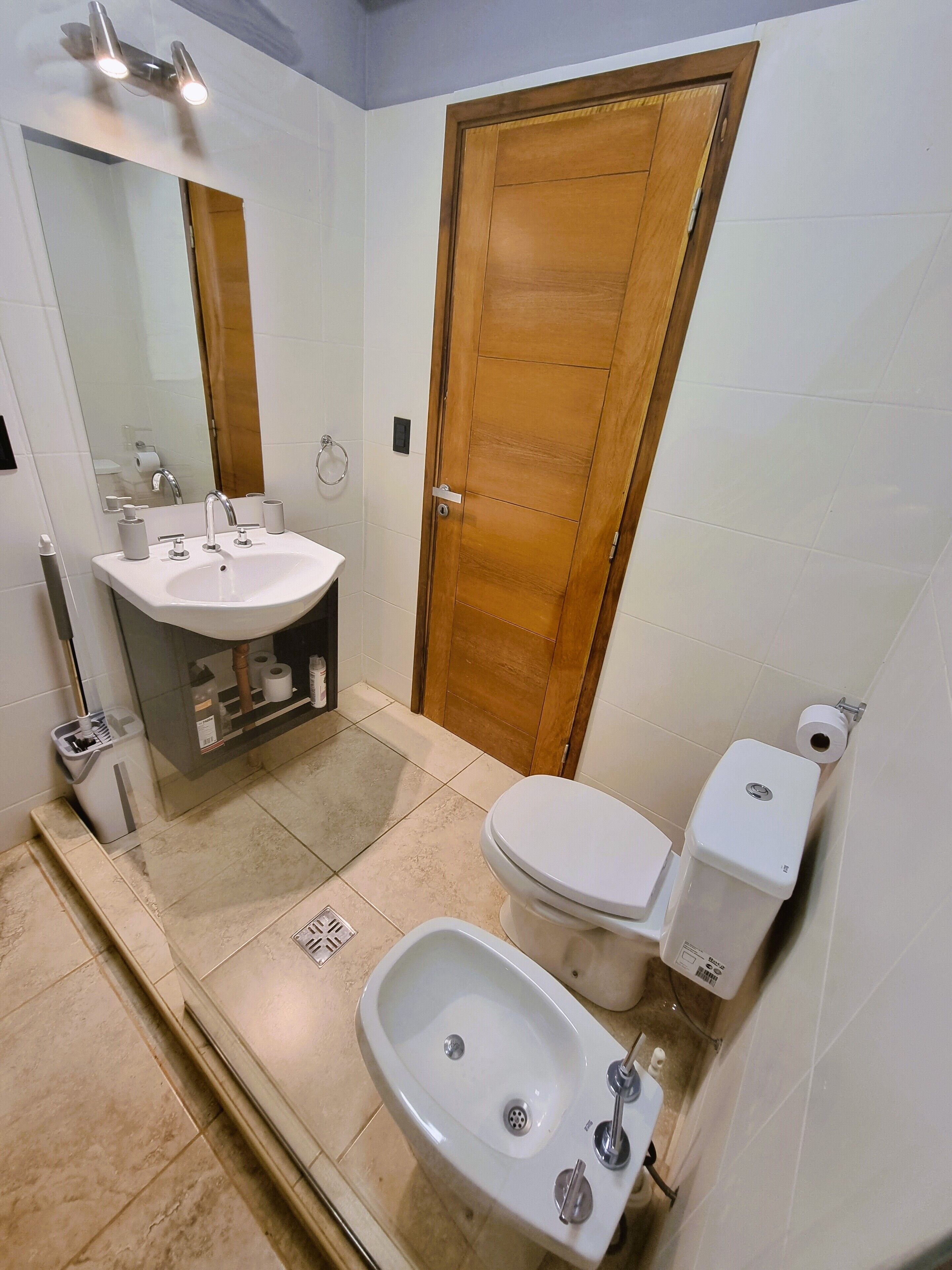A bathroom with a sink, toilet, bidet, and a wooden door.