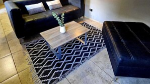 A modern living room with a black leather sofa, a wooden coffee table, and a patterned rug. - Drummond Apartments (Luján de Cuyo)