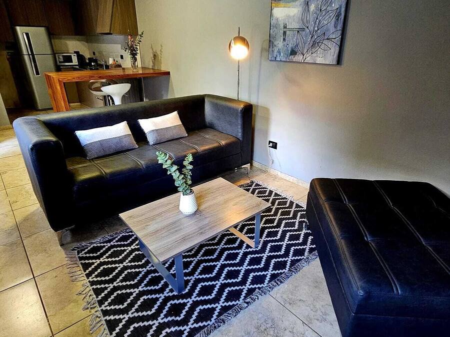 Una sala moderna con un sofá de cuero negro, una mesa de centro de madera y una alfombra estampada.