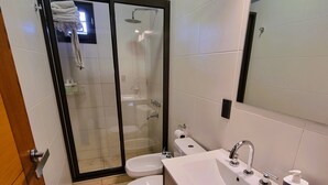 A modern bathroom with a glass-enclosed shower, a white sink with a black cabinet, and a toilet. - Drummond Apartments (Luján de Cuyo)