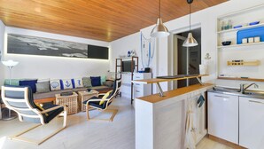 Eine moderne Küche mit Holzbalkendecke, einem Essbereich mit Sofa und Sesseln sowie einer Kücheninsel mit Spüle und Schränken.