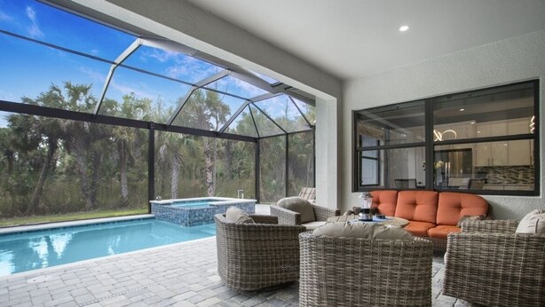 A modern outdoor living area with a pool, wicker furniture, and a glass-enclosed patio. - Casa Campagnola Naples heated pool h.tub outdoor kitchen 2 bikes  (Naples)