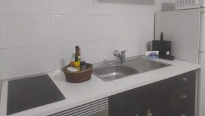 A kitchen with white tiles, a stainless steel sink, a microwave, and a basket of condiments. - Ginjals-67 (Almargem do Bispo)