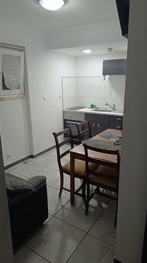 A dining area with a table and chairs, a kitchen in the background, and a tiled floor. - Ginjals-67 (Almargem do Bispo)