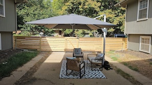 Un patio al aire libre con una mesa, sillas, un paraguas grande y un tapete estampado.