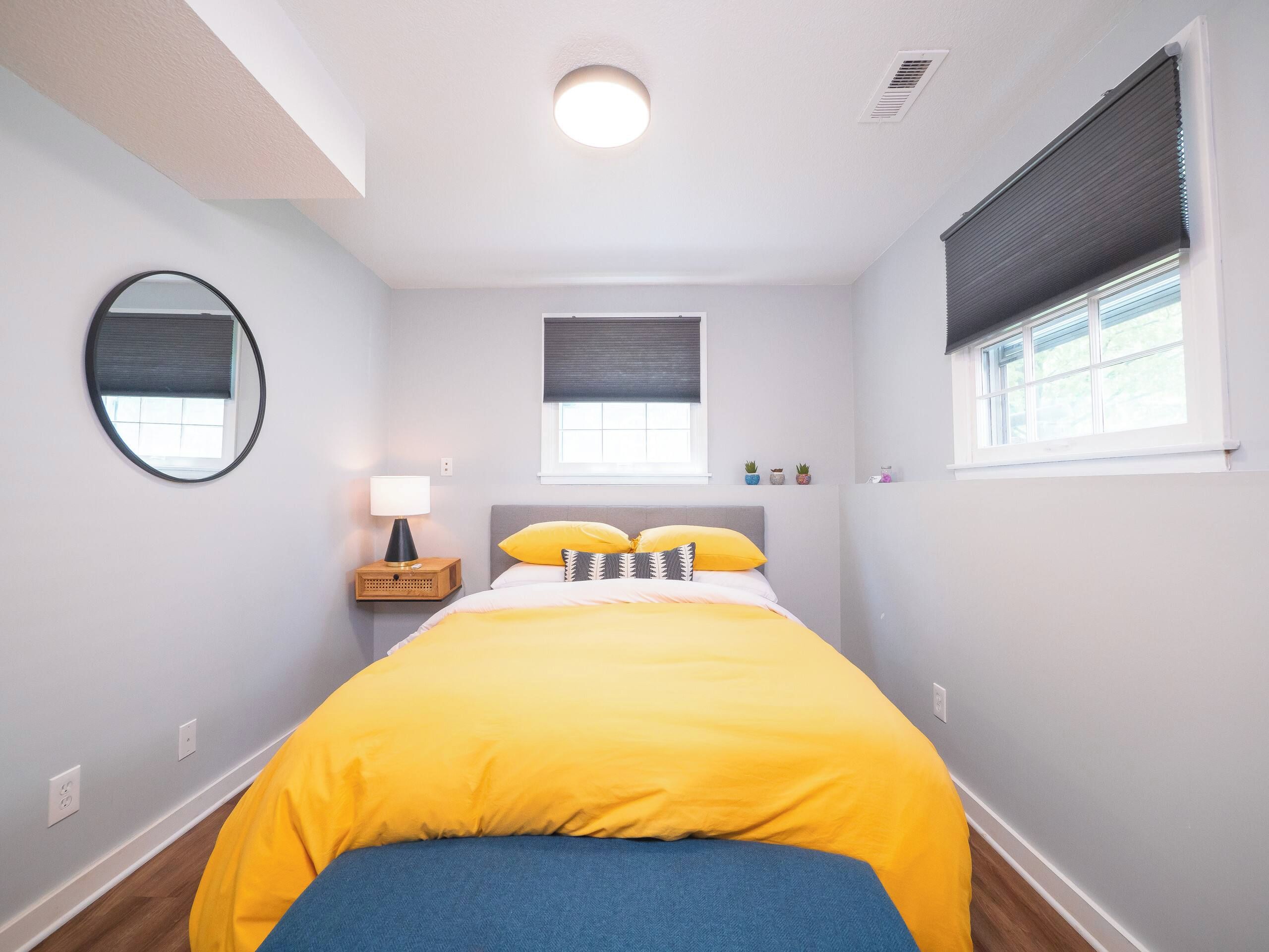 A bedroom with a bed, bedside table, lamp, and a window with blinds.