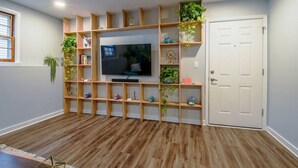 Ein Zimmer mit Fernseher an einer Holzwandregal-Konstruktion, Holzdielenboden und einer weißen Tür.