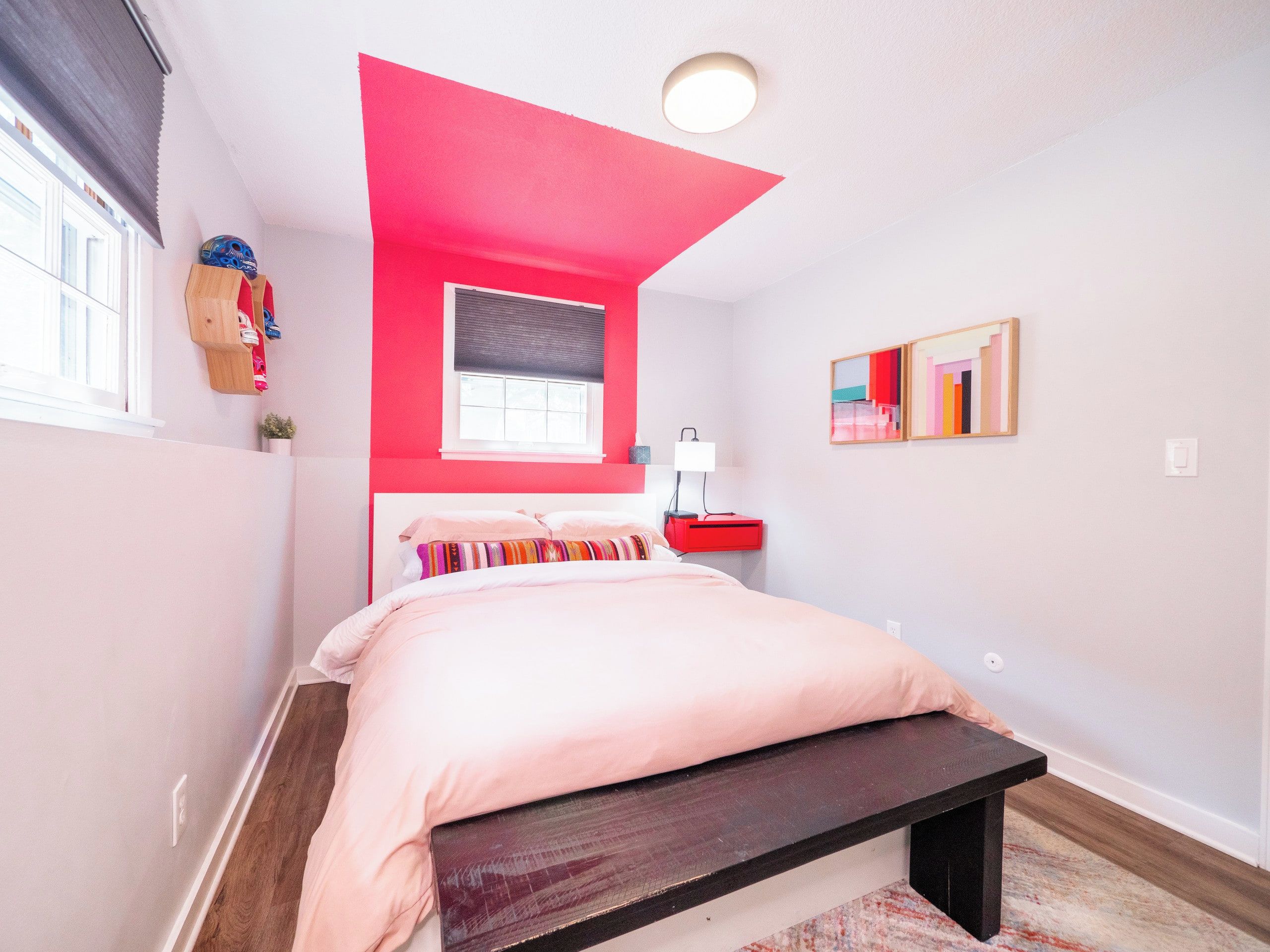 Ein Schlafzimmer mit einem Bett, einem Nachttisch, einer Lampe, einem Fenster und einem an der Wand befestigten Regal.