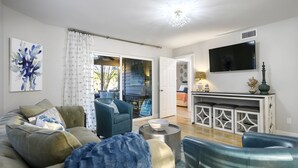 A living room with a sofa, chairs, a coffee table, a TV, and a sliding glass door leading to an outdoor area. - Lakefront Sandestin Home w/ Golf Cart &Arcade Room (Mir)