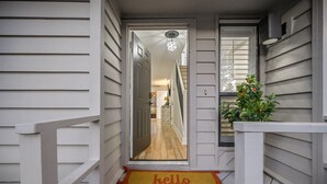 A house entrance with a wooden door, a hallway leading inside, and a 'hello sunshine' mat at the bottom. - Lakefront Sandestin Home w/ Golf Cart &Arcade Room (Mir)