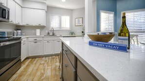 A modern kitchen with white cabinets, a stainless steel oven, a microwave, and a sink. There is a wicker basket on the counter and a bottle of wine. - Lakefront Sandestin Home w/ Golf Cart &Arcade Room (Mir)