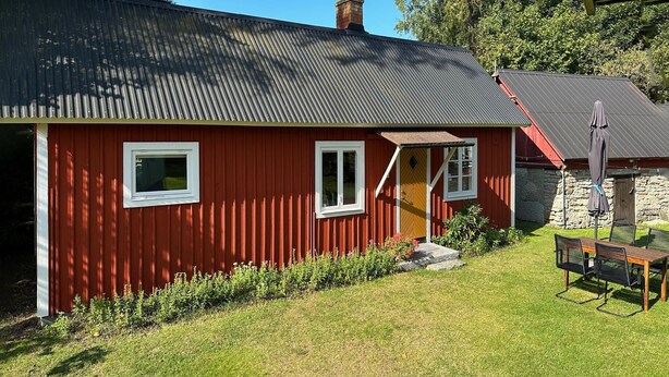 Una casa de madera roja con techo gris, un pequeño porche y un muro de piedra.