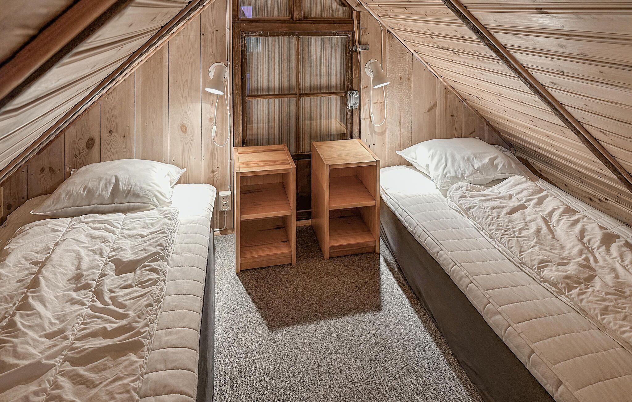 Una habitación pequeña y acogedora con dos camas individuales, un escritorio de madera con estantes y una ventana.