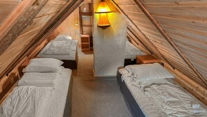 Un dormitorio en ático acogedor con cuatro camas dispuestas en forma de U, una lámpara central y una escalera de madera que lleva a una zona superior.