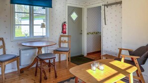 Una habitación acogedora con una mesa de madera, dos sillas, un radiador, un ventanal con vistas y una puerta que da a otra habitación.
