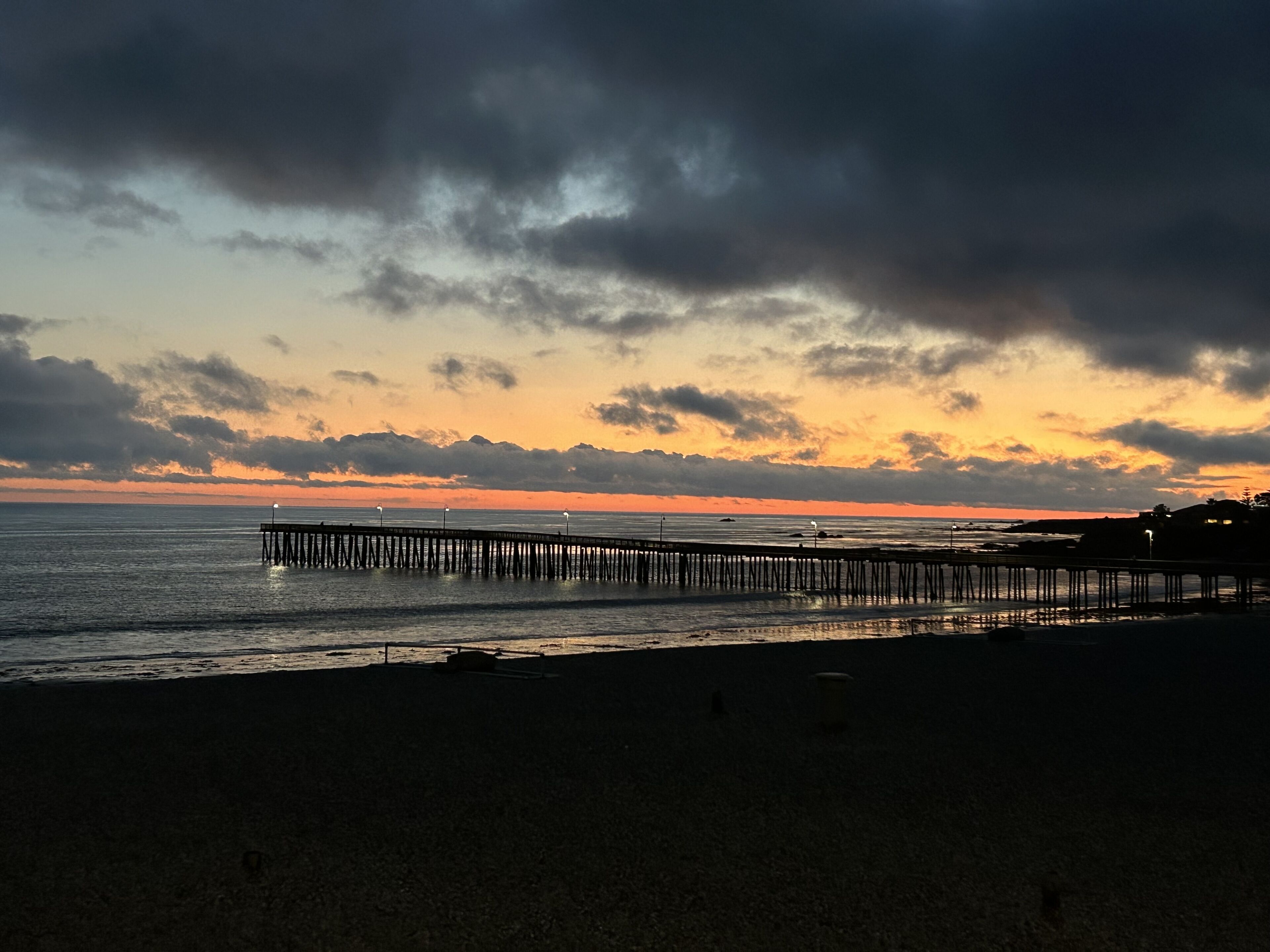 A pier extending into calm waters with a sunset in the background.